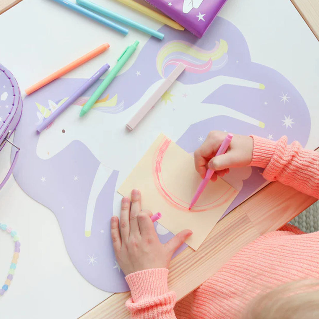 Een kind tekent op papier dat op de A Little Lovely Company eenhoorn placemat ligt.
