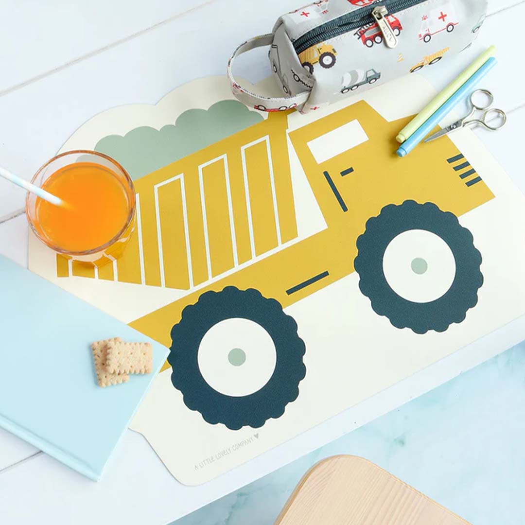 Een gele kiepwagen placemat van A Little Lovely Company ligt op tafel met een glas sap en koekjes.
