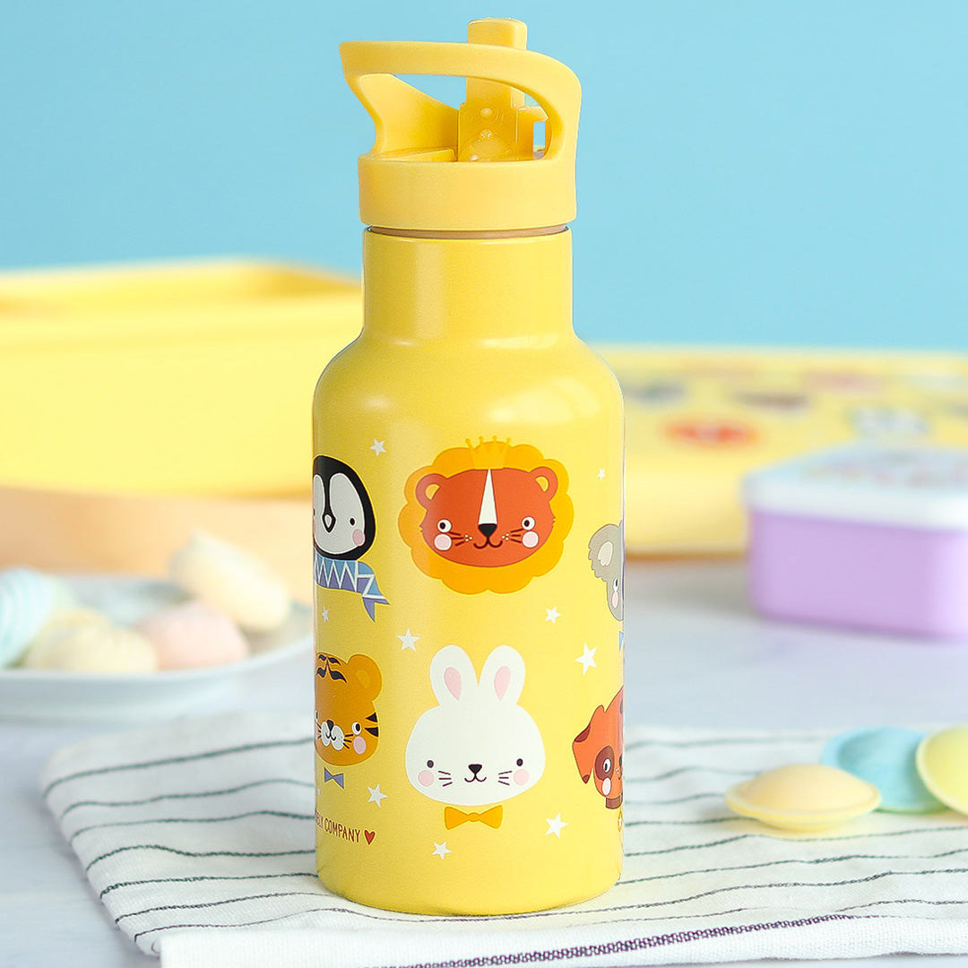 Een gele a little lovely company kinder drinkfles met dierenvrienden en sterren op een gestreepte doek met lunchbox.