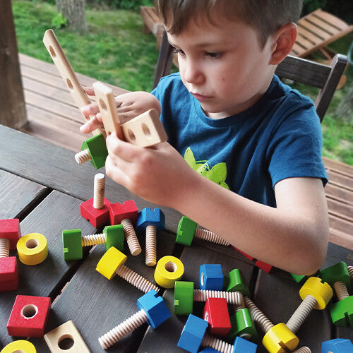 Een jongen bouwt geconcentreerd met de houten bouten, moeren en planken van de constructieset.