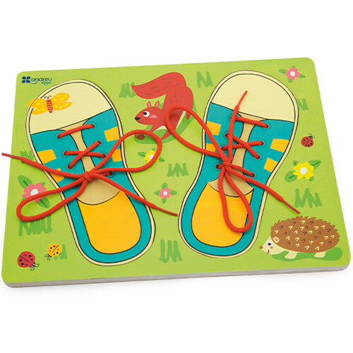 Bovenaanzicht van de Andreu Toys houten puzzel om veters te strikken, met beide schoenen op de groene ondergrond.