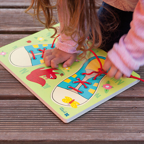 Een kind leert veters strikken met de Andreu Toys houten puzzel op een houten ondergrond.