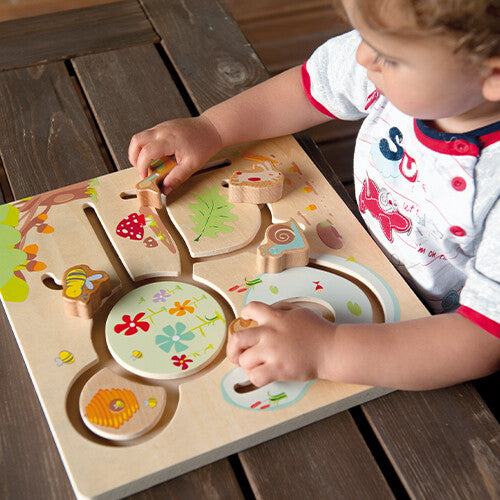 Een peuter speelt met de houten schuifpuzzel met bosdieren op een houten tafel.