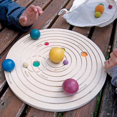 Een kind speelt met het houten zonnestelselmodel op een houten tafel.