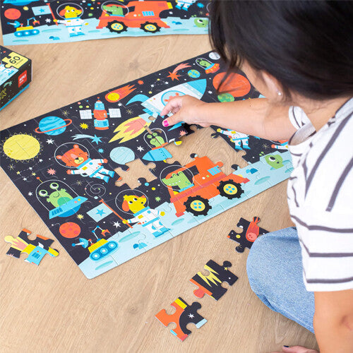 Een persoon die een deel van de ruimte-legpuzzel met 60 stukjes in elkaar zet op een houten vloer.