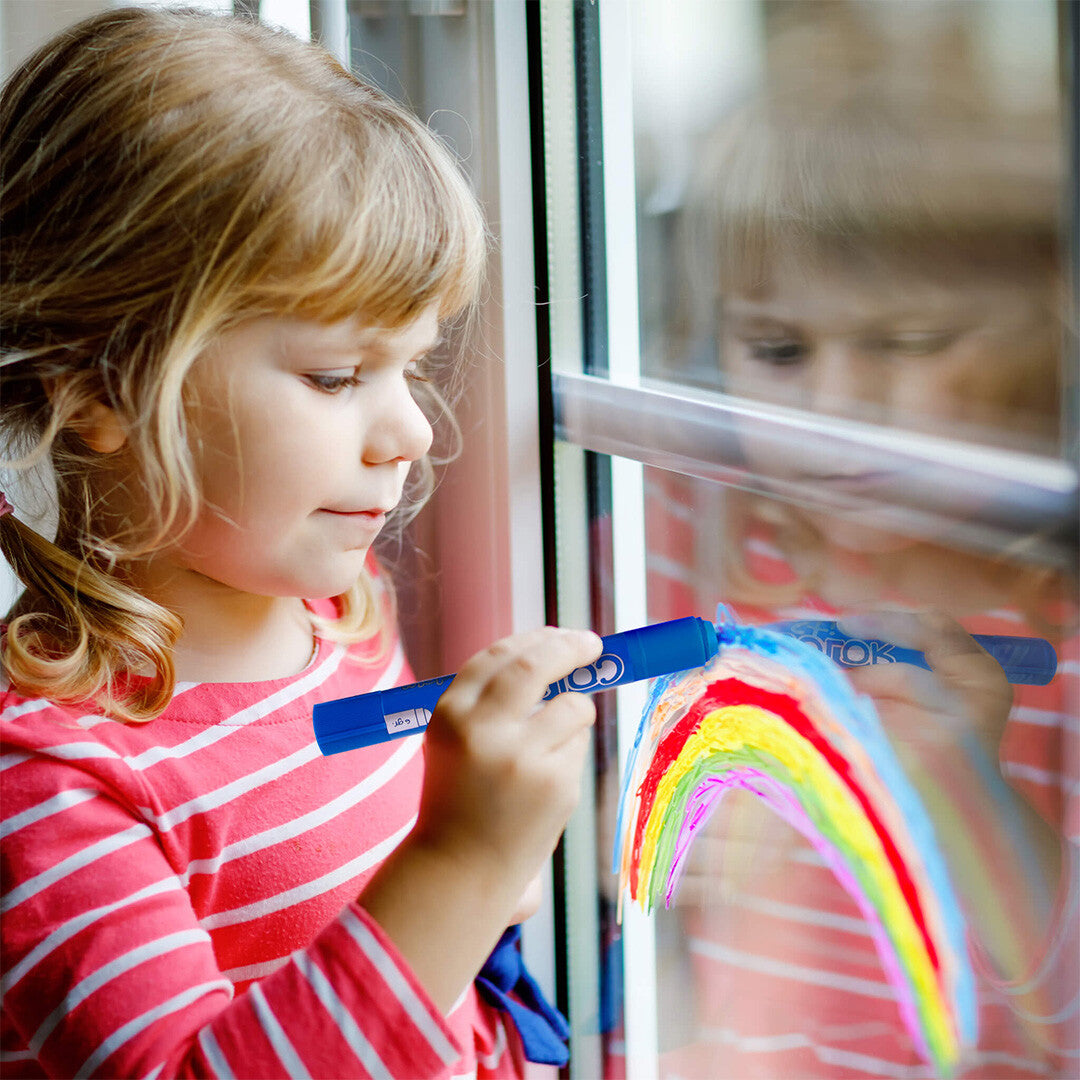 Een kind tekent een regenboog op een raam met een blauwe APLI kids verfstift.
