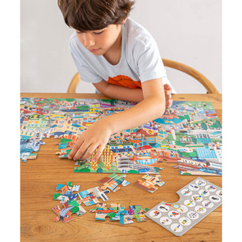 Een kind legt de APLI Kids legpuzzel met een drukke stadsafbeelding op een houten tafel.