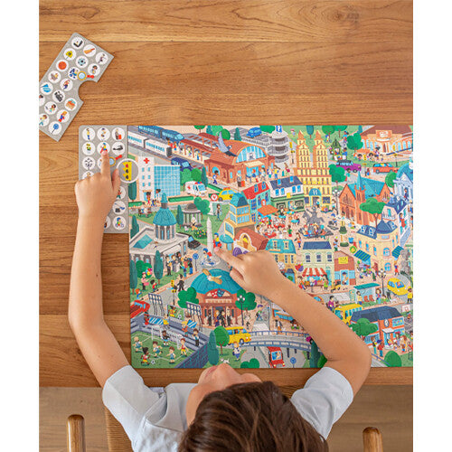 Een kind wijst naar details op de APLI Kids observatie legpuzzel met een stadsafbeelding en naar een observatiekaart.