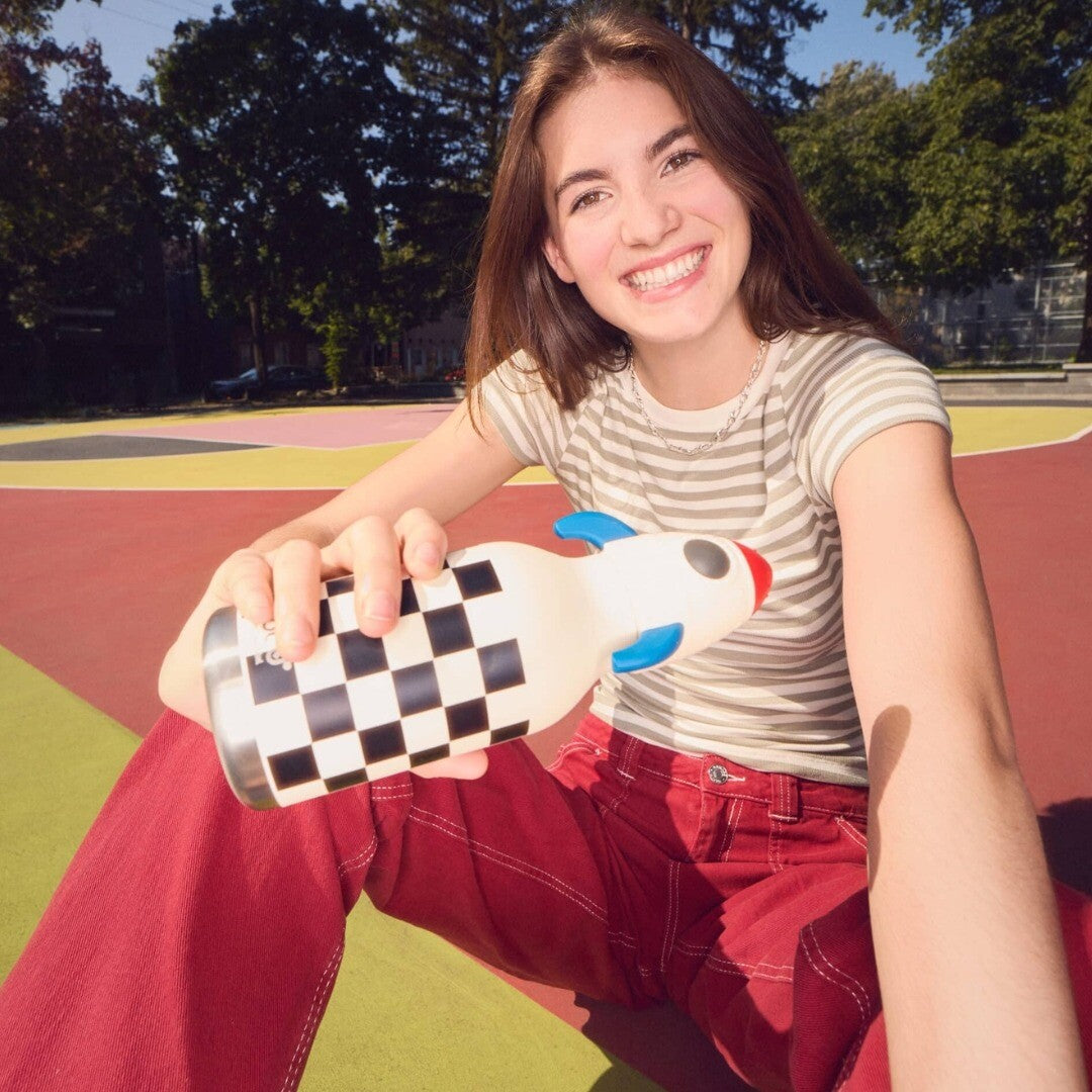 Een lachende jonge vrouw houdt de asobu rvs drinkfles met raketdop en geruit patroon vast.