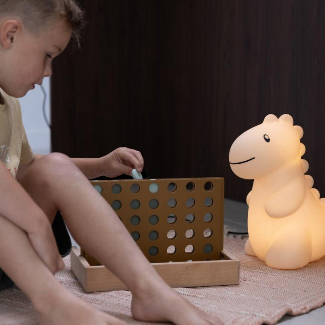 Een kind speelt een spel op de grond naast de zandkleurige dino kinderlamp.
