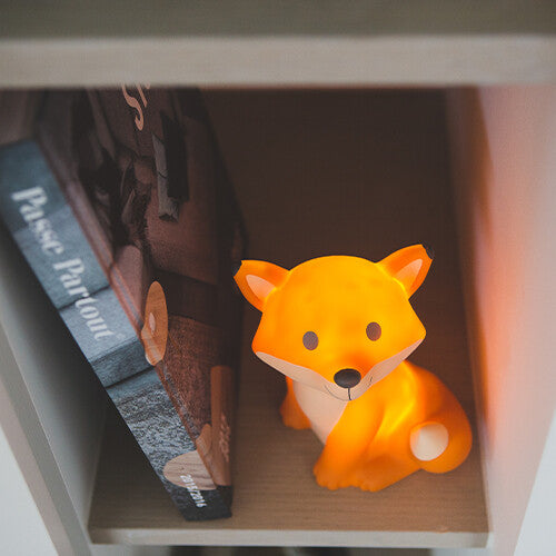 Brandend Atelier Pierre LED nachtlampje in de vorm van een vos, op een plank naast een boek.