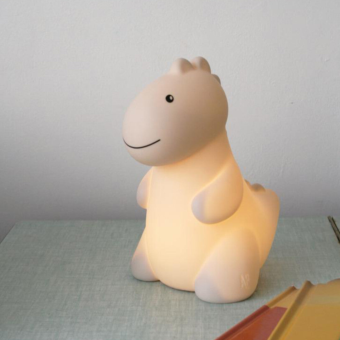 Atelier Pierre dino nachtlampje dat warm licht geeft, staand op een nachtkastje.
