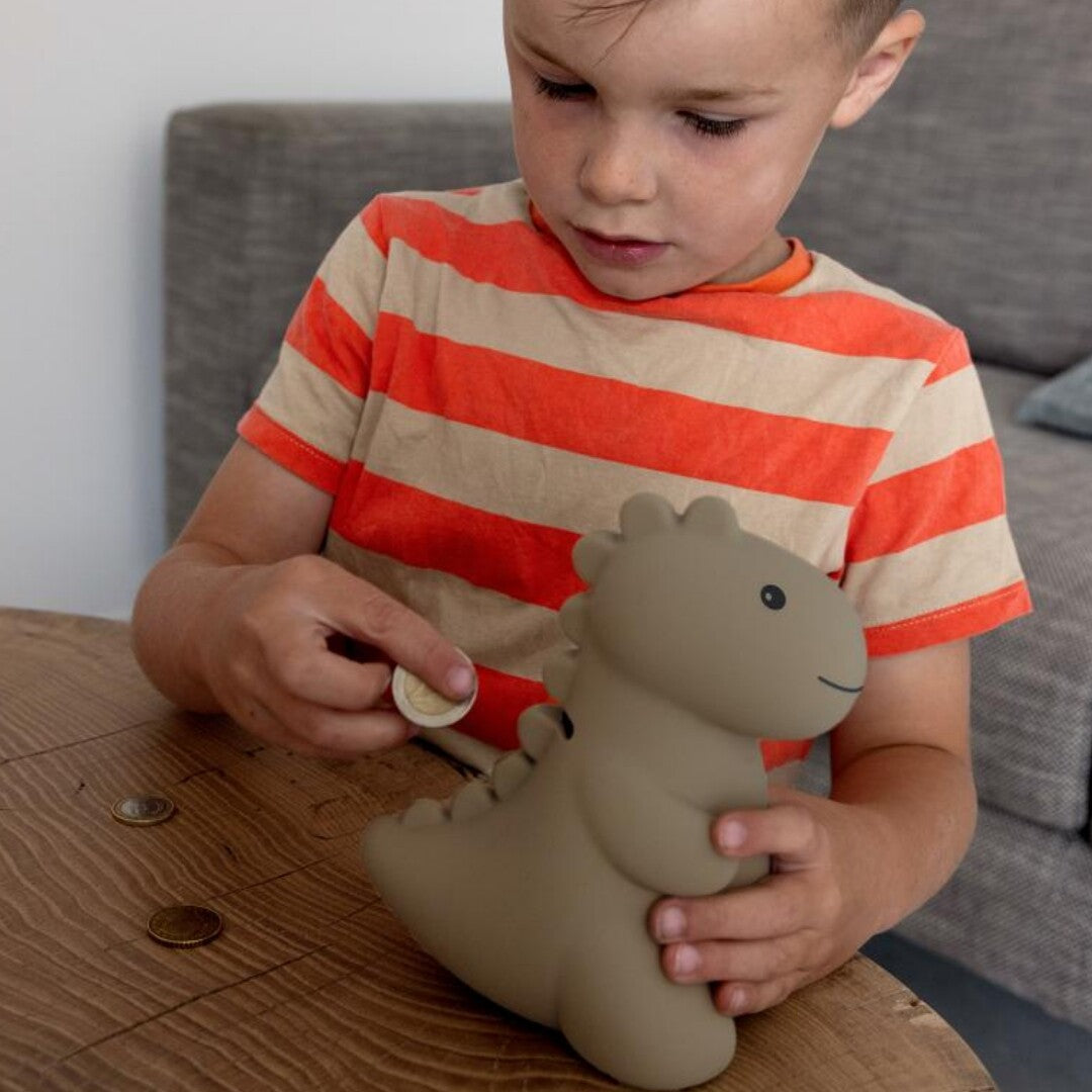 Een kind stopt een munt in de beige dino spaarpot.