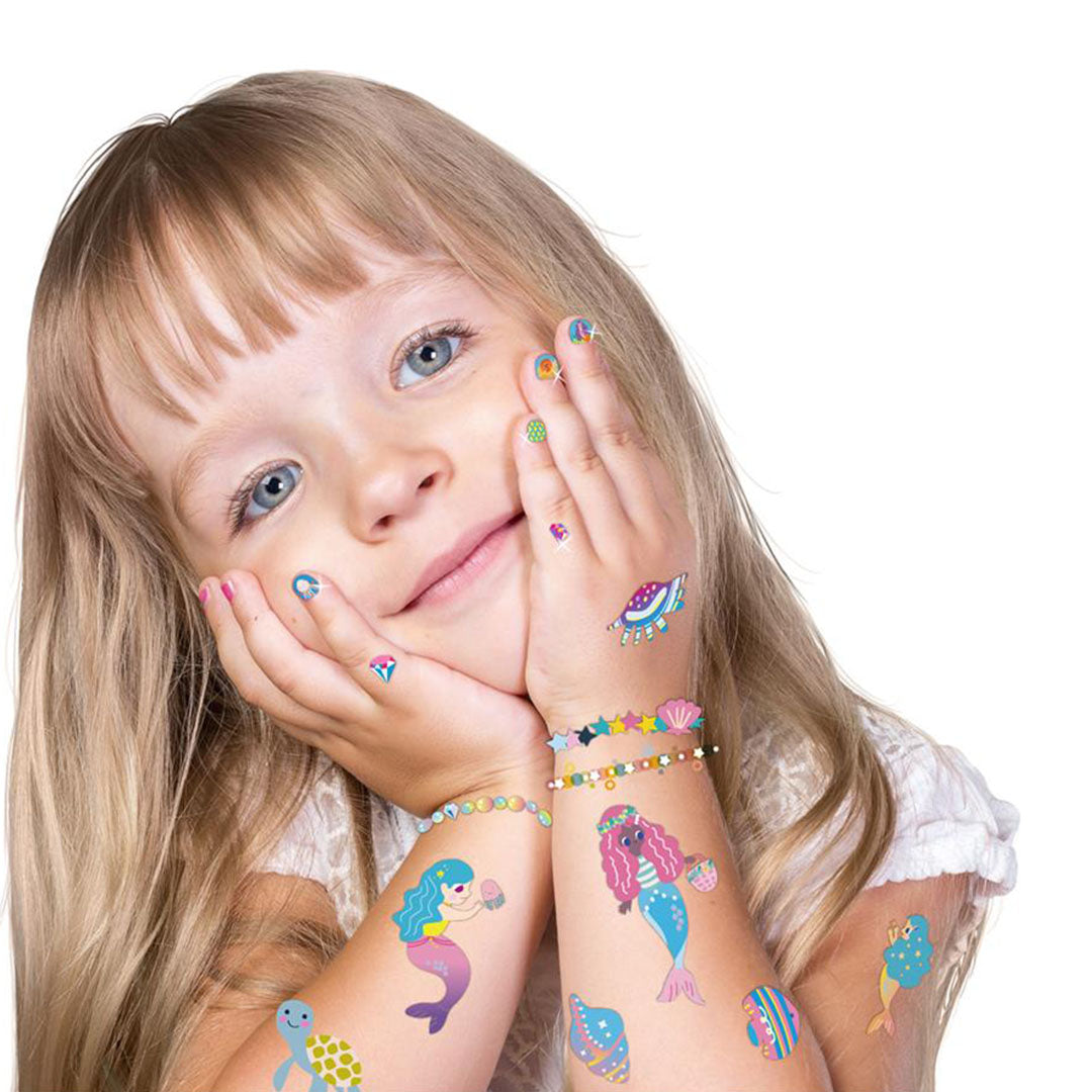 Een meisje met zeemeermin-nagelstickers en tijdelijke tattoos op haar armen en handen.