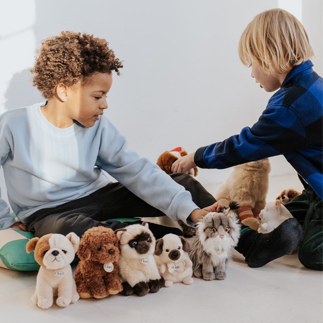 Twee kinderen zitten op de grond en spelen met een collectie b.t. chaps pluchen knuffeldieren, waaronder de Noorse boskat.
