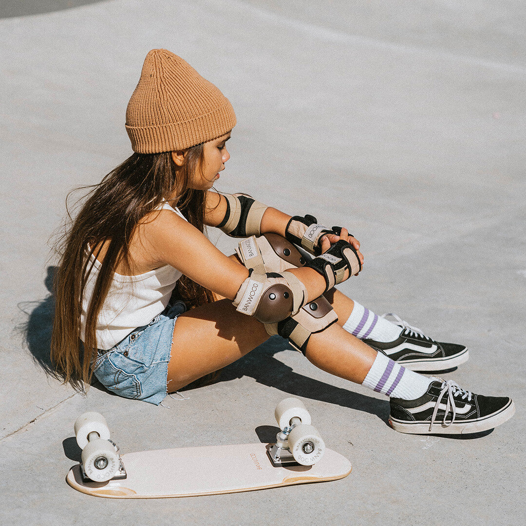 Een kind zit op de grond met de Banwood beschermingsset aan en een skateboard ernaast.