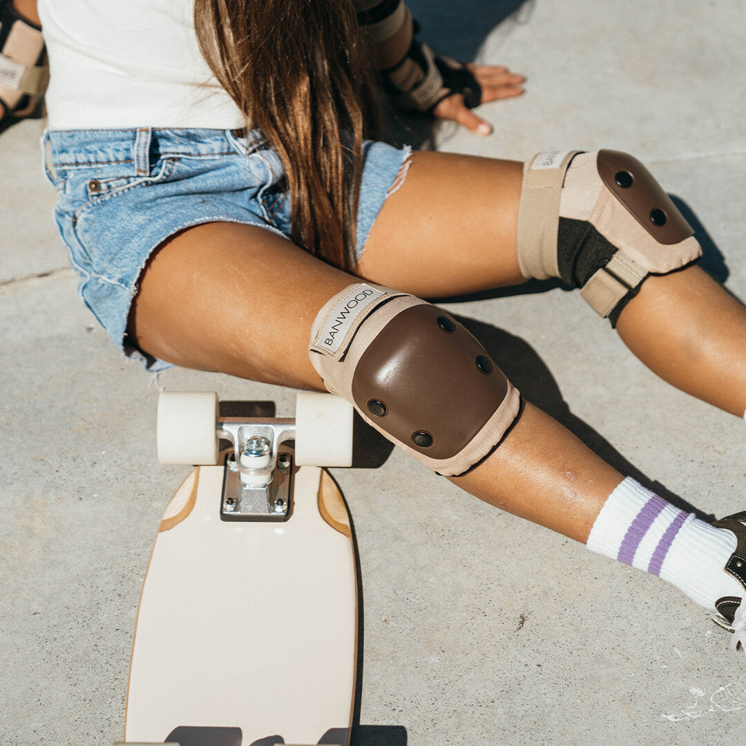 Detail van de Banwood kniebeschermers op de knieën van een kind dat naast een skateboard zit.