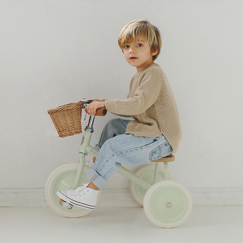 Een jong kind rijdt op de Banwood mintgroene driewieler met rieten mandje.