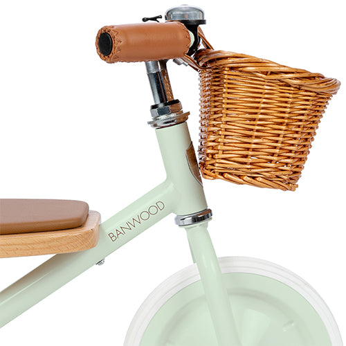 Detail van de voorkant van de Banwood mintgroene driewieler met stuur, bel en rieten mandje.