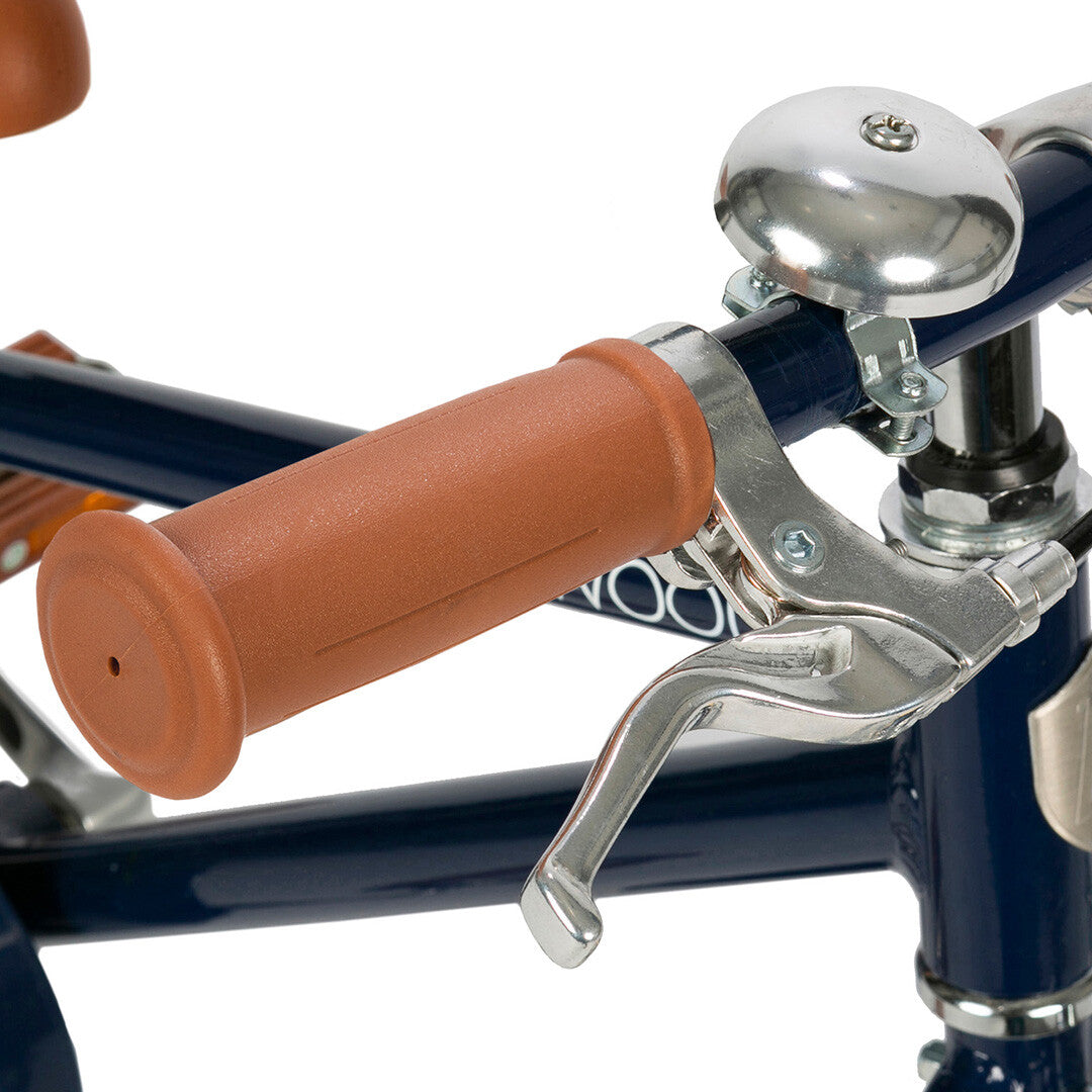 Detail van het stuur van de kinderfiets met bruine handgreep, zilveren rem en bel.