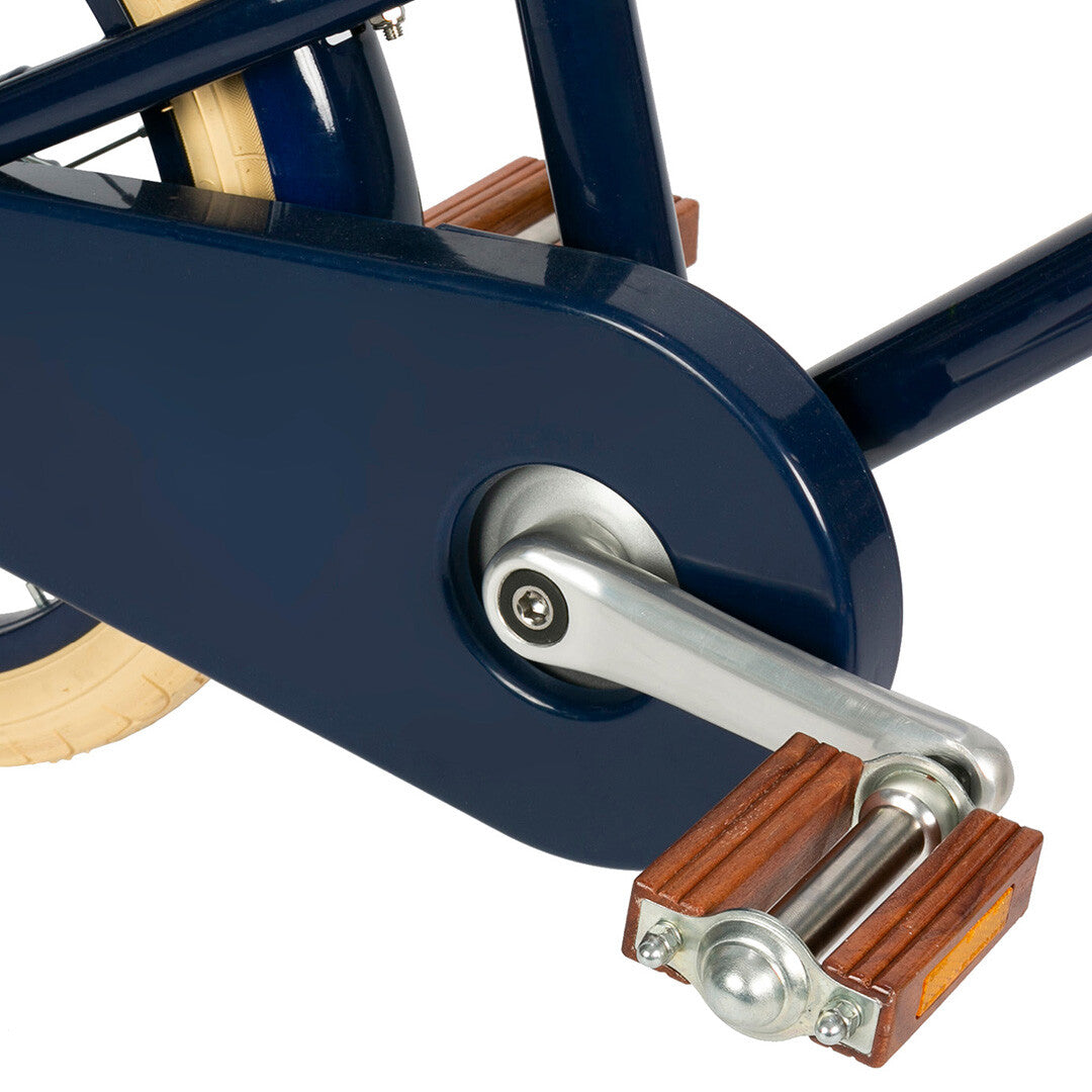 Detail van de donkerblauwe kettingkast en het pedaal met houten afwerking van de kinderfiets.