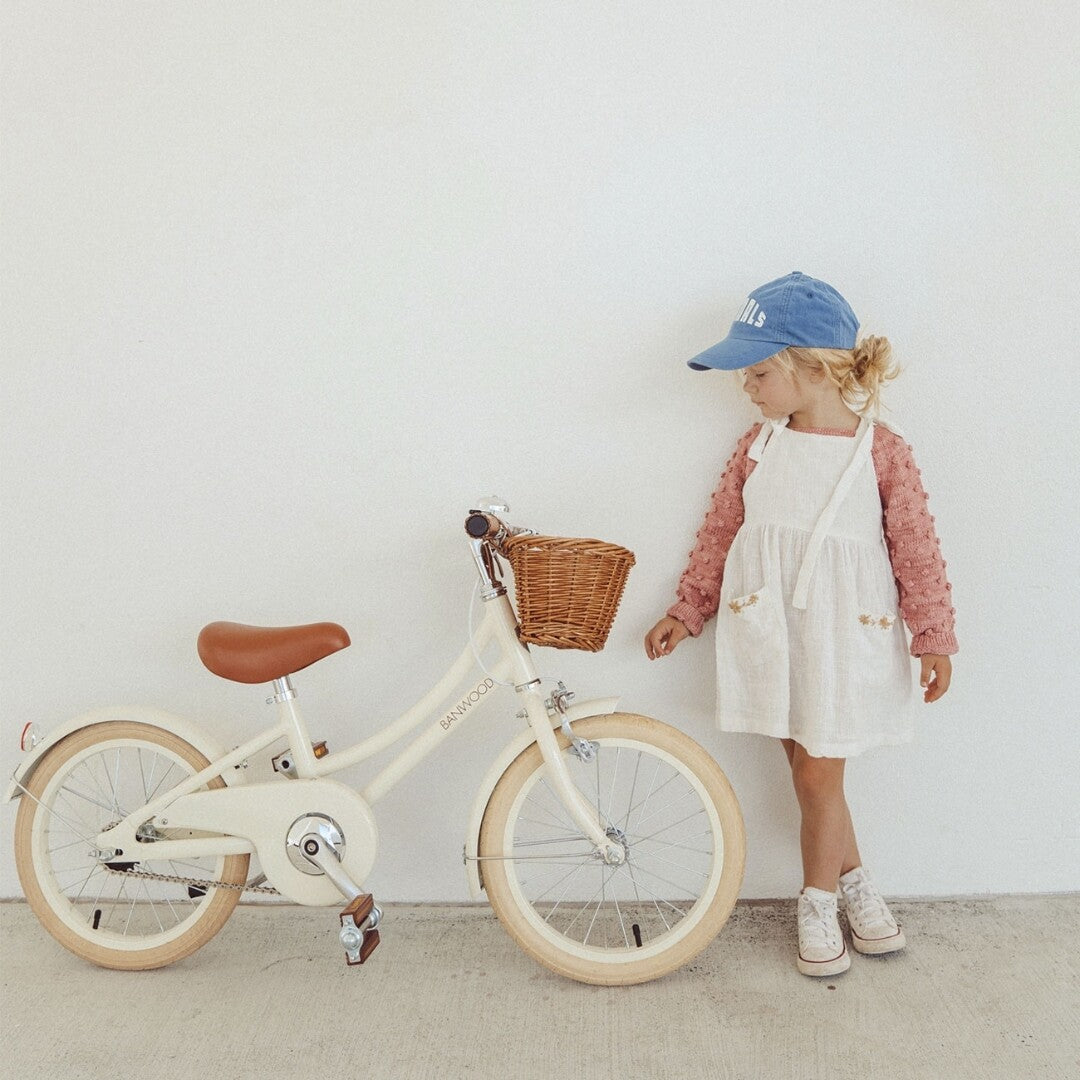 Een kind staat naast de crèmekleurige Banwood kinderfiets met rieten mandje.