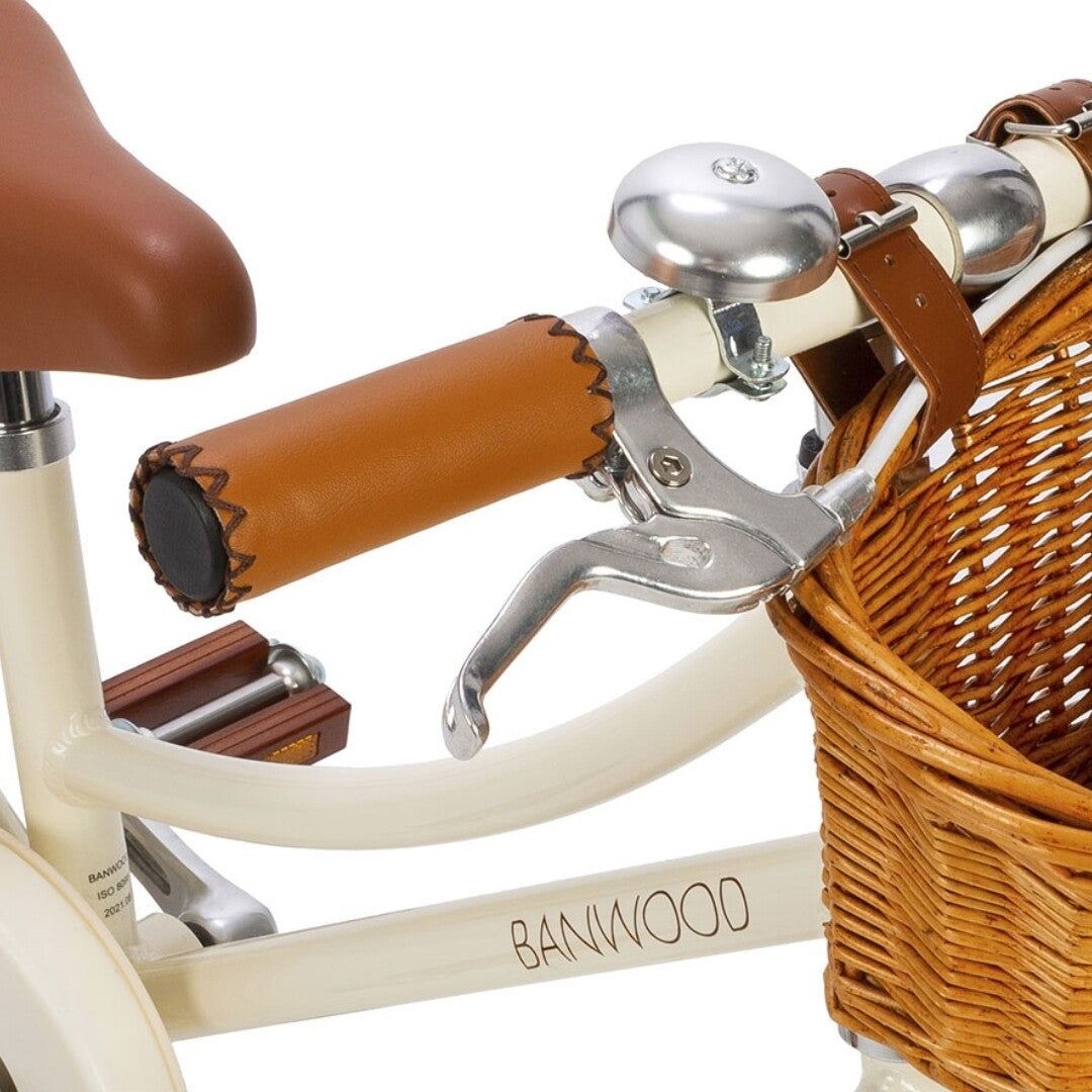 Detail van de Banwood kinderfiets met bruine handvatten, zilveren bel en rieten mandje.