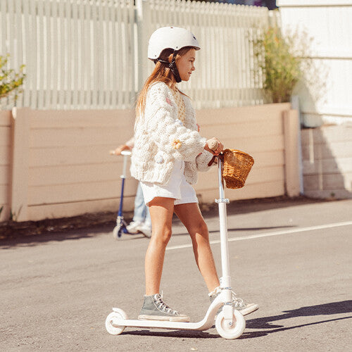 Een kind met helm rijdt op een crème Banwood kinderstep maxi met mandje op straat.