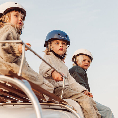 Drie kinderen dragen Banwood kinderhelmen, zittend op een autodakrek.