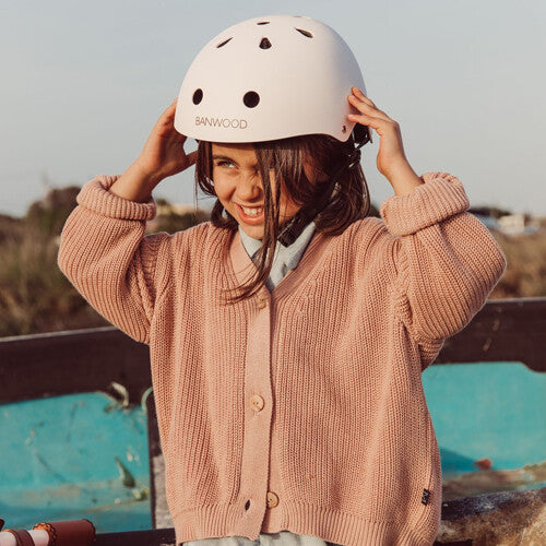 Een lachend meisje met een roze Banwood kinderhelm op haar hoofd.