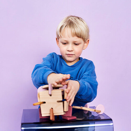 Een jongen speelt met een bavvic houten bouwspeelgoed met roze en bruine siliconen connectors.