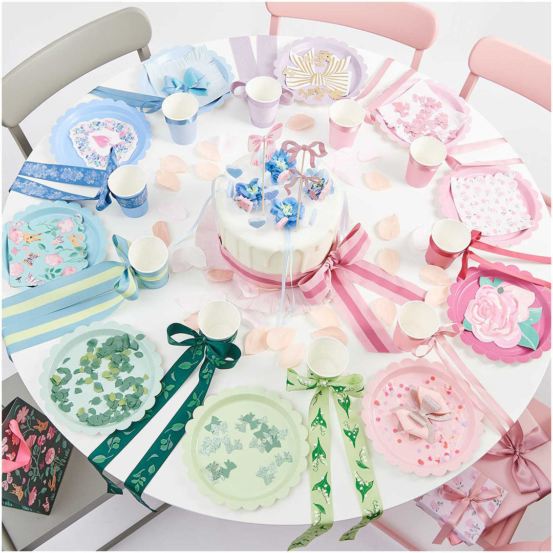 Een feestelijk gedekte tafel met een verjaardagstaart en diverse pastelkleurige feestartikelen, waaronder papieren bekers.