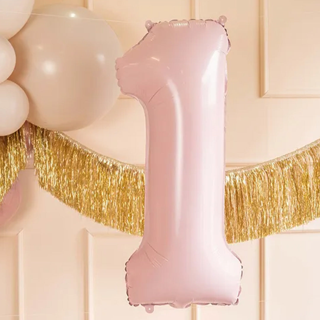 Lichtroze cijferballon 1 hangend als feestdecoratie tegen een roze muur met andere ballonnen en een gouden slinger.