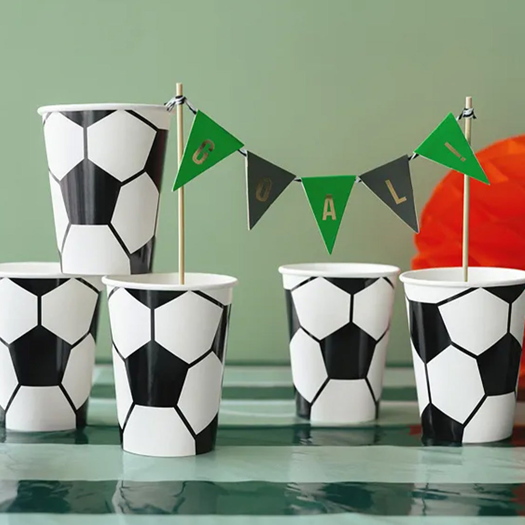 Meerdere partydeco papieren voetbal feestbekers op een tafel met een 'GOAL' slinger.