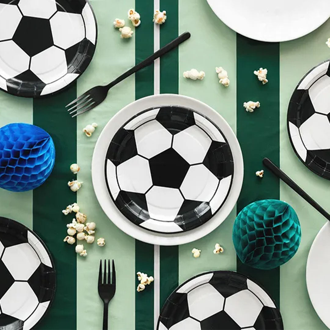 Een feesttafel met partydeco voetbal feestbordjes, popcorn en decoraties op een groen-wit gestreepte ondergrond.
