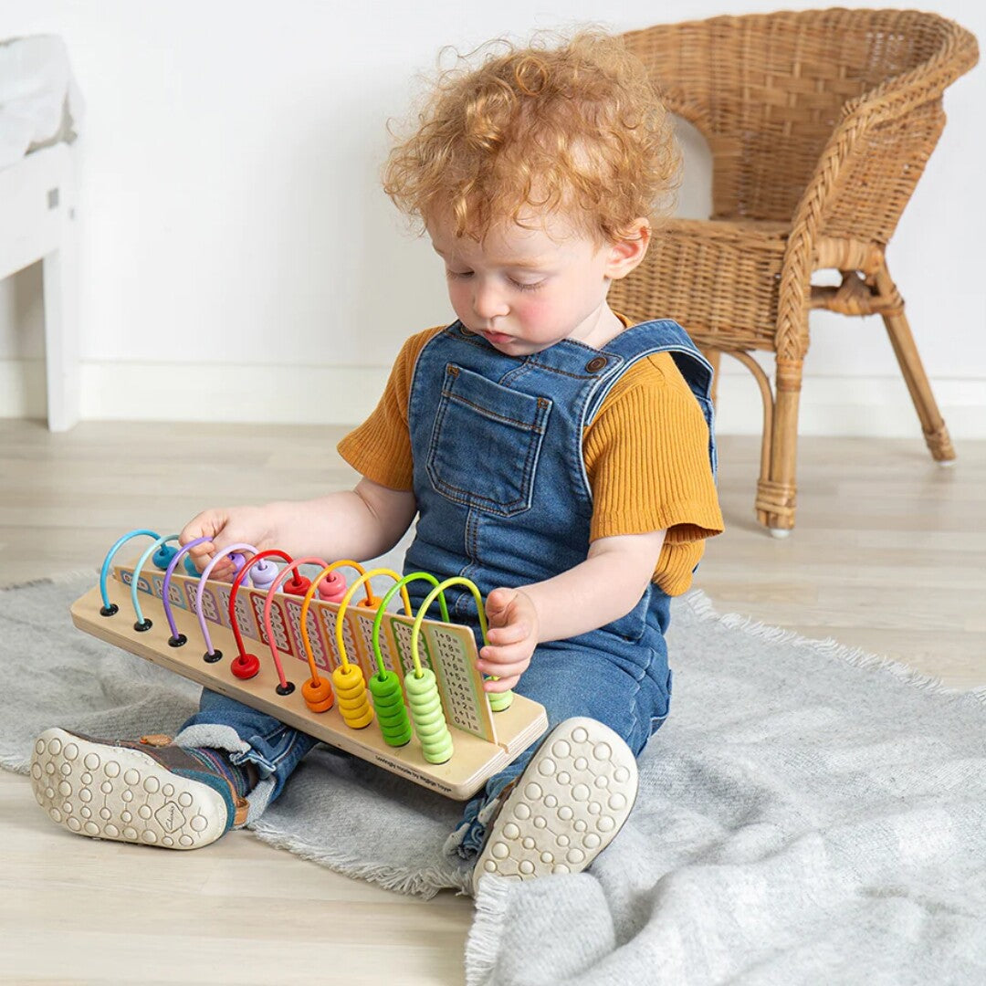 Een jong kind zit op de grond en speelt met het Bigjigs regenboog telraam.