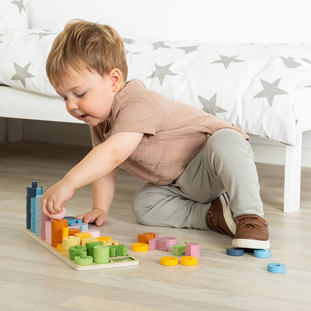 Een peuter speelt geconcentreerd met het Bigjigs houten telspel counting board op de vloer.