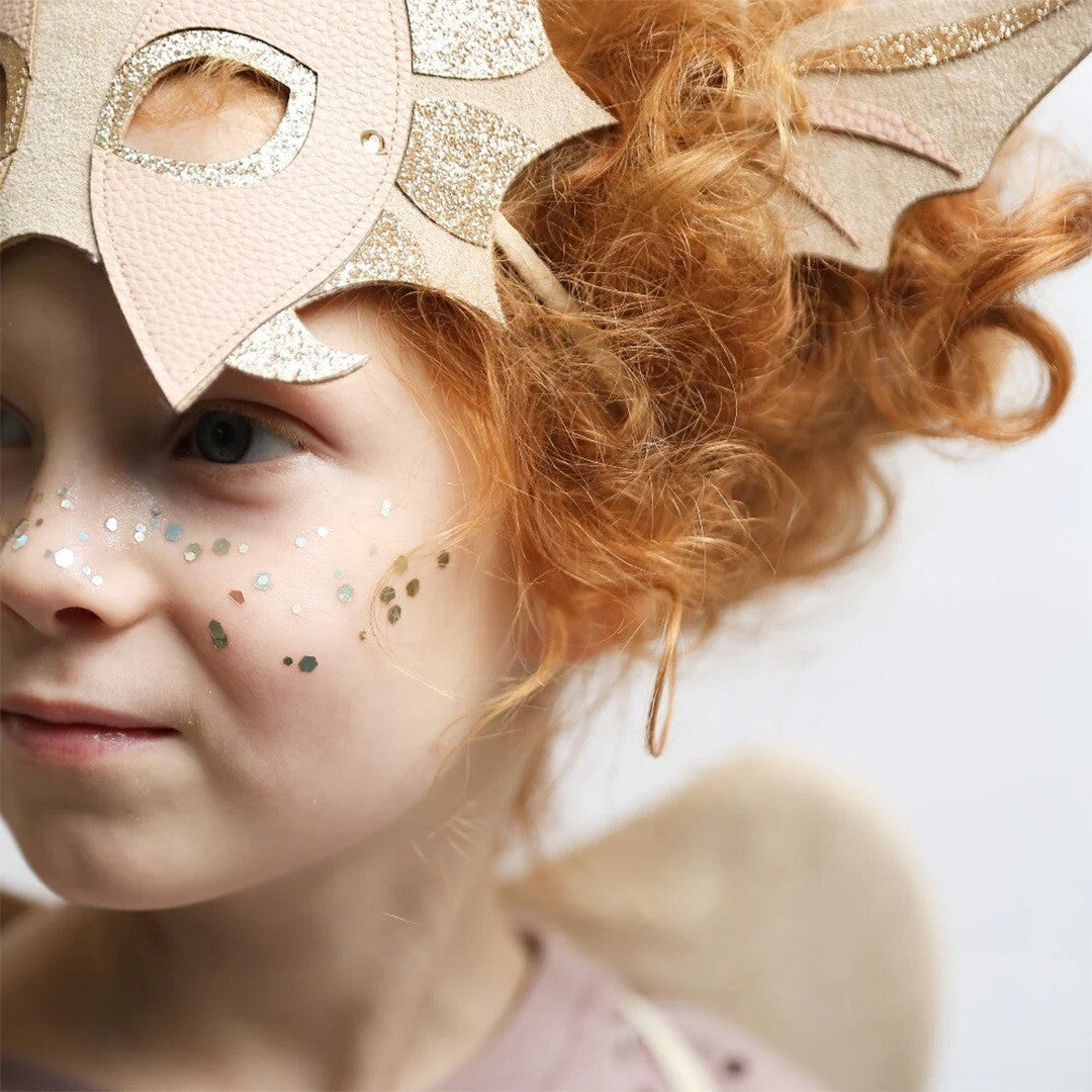 Kind met rood haar draagt de draken oren hoofdband en heeft glitter op de wangen.