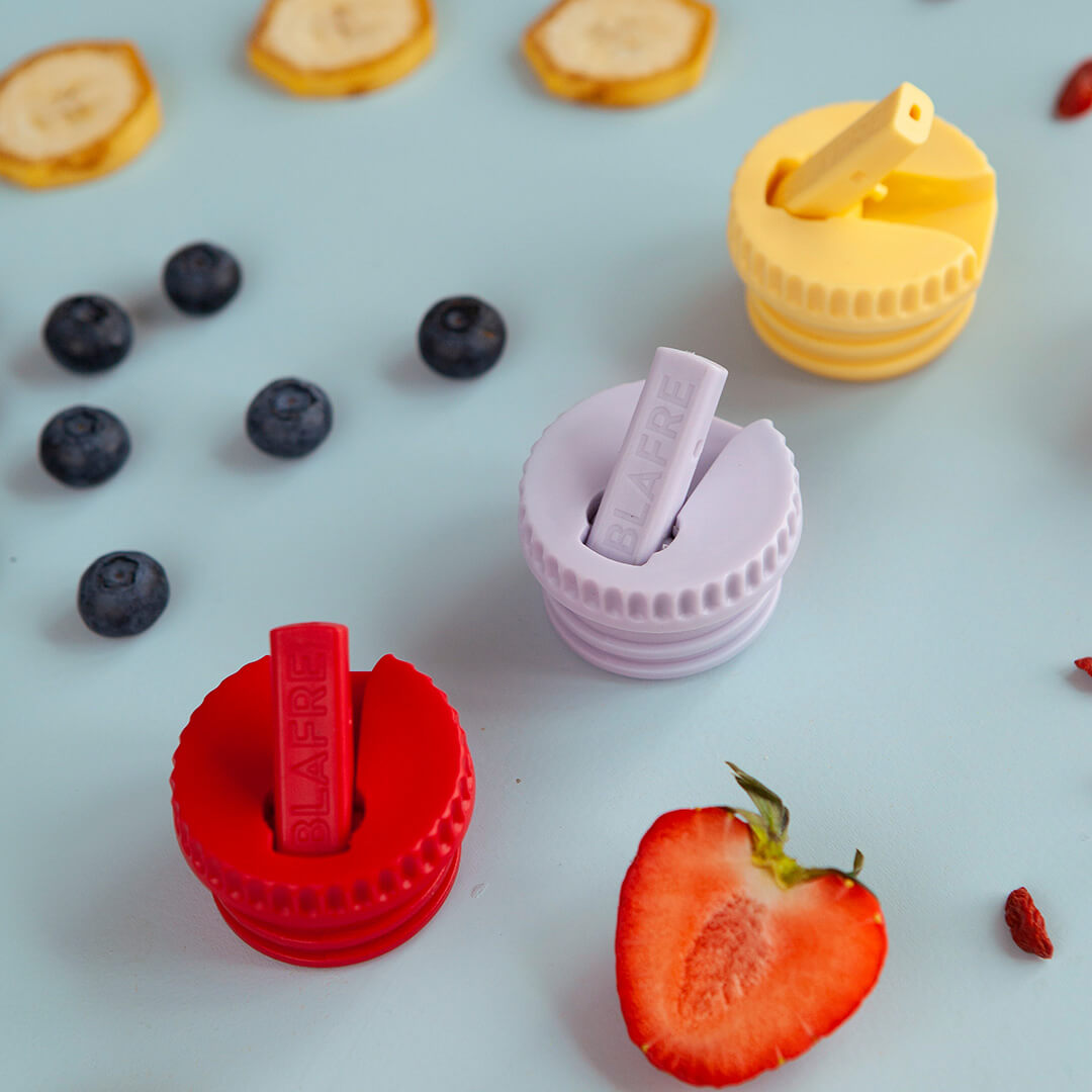 Drie Blafere doppen met drinktuit in rood, lila en geel, omringd door fruit.