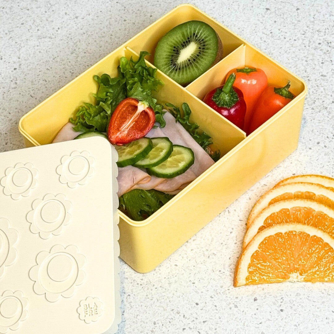 Open Blåfre kinderlunchbox met bloemenpatroon, gevuld met een lunch.