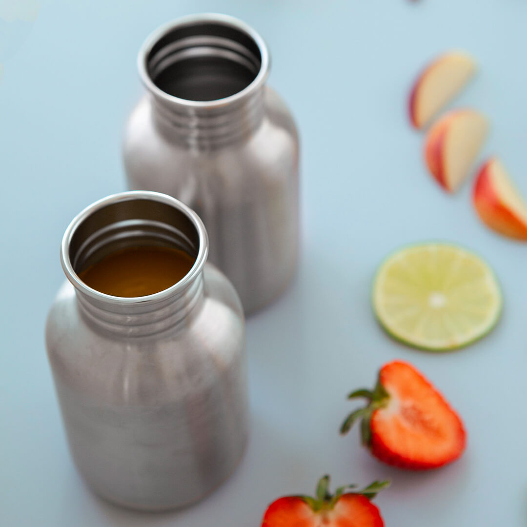 Twee Blafere roestvrijstalen drinkflessen zonder dop, omringd door gesneden fruit.