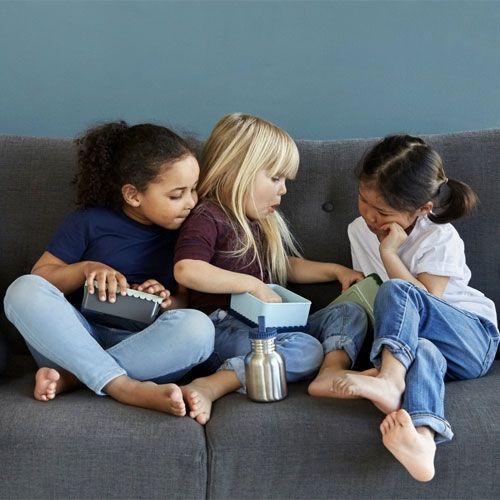 Drie kinderen zitten op een bank met een Blåfre roestvrijstalen waterfles en lunchboxen.