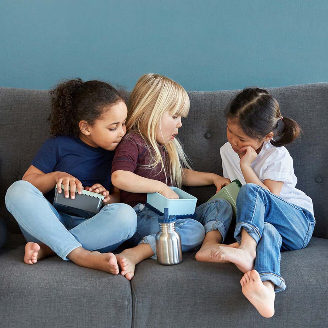 Drie kinderen zitten op een bank met lunchboxen en een Blåfre roestvrijstalen drinkfles.