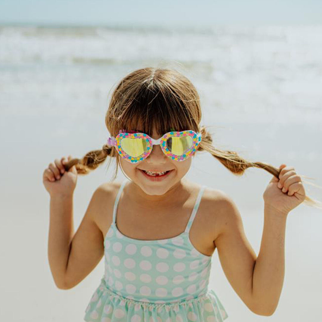 Een meisje met vlechtjes draagt de bling2o kinder zwembril met hartjesglazen op het strand.