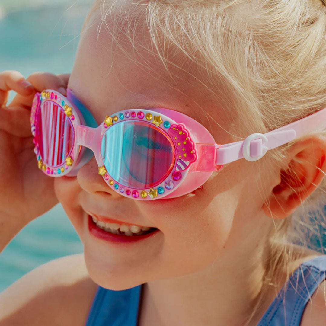 Een lachend kind draagt de bling2o kinderzwembril Candy Carnival met roze en blauwe glazen bij het zwembad.