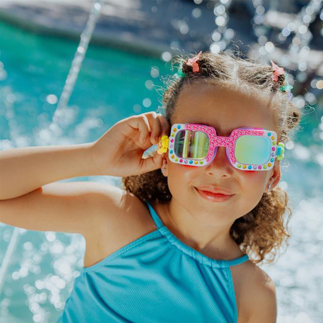 Een lachend meisje draagt de bling2o zwembril voor kinderen bij een fontein.