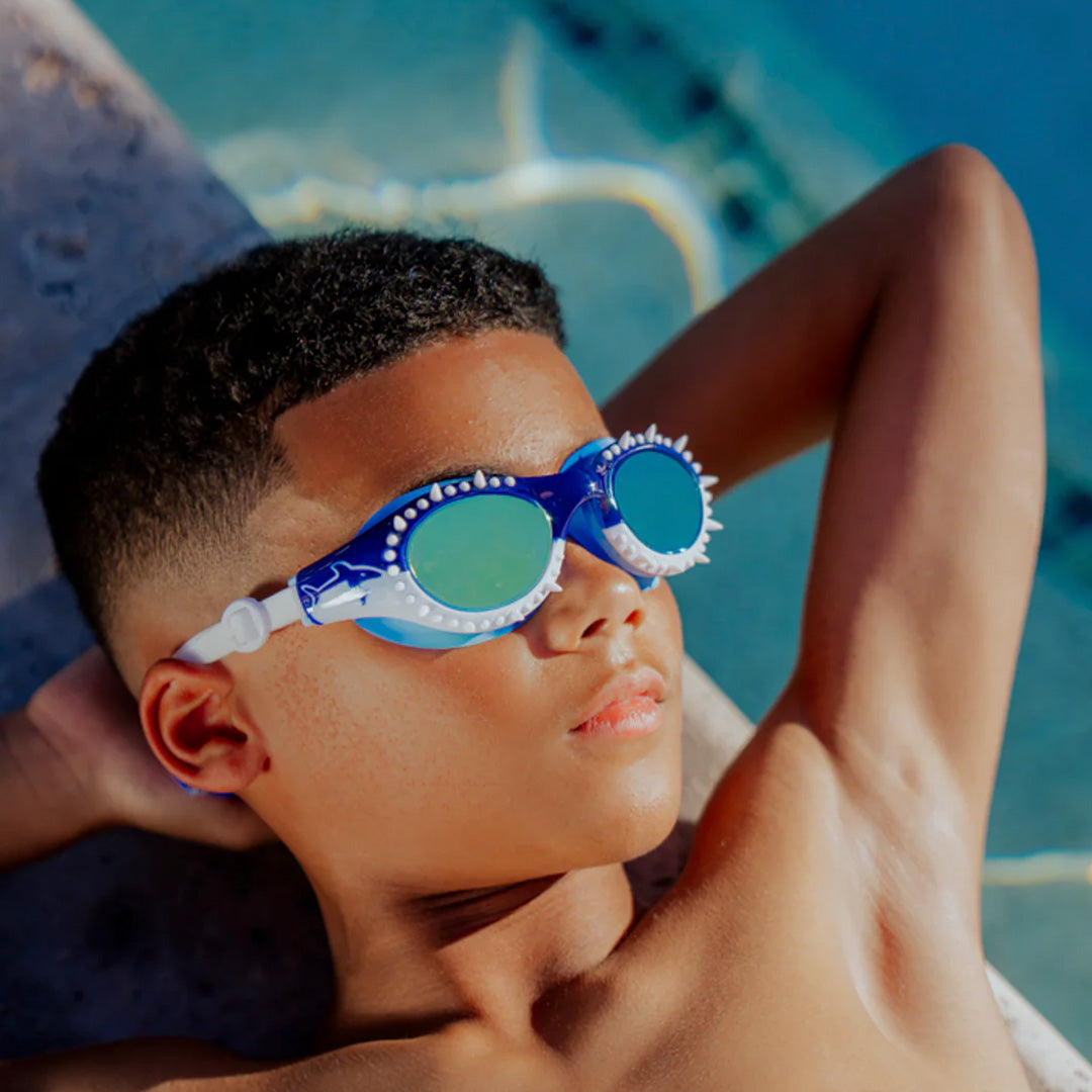 Kind draagt de blauwe bling2o kinderzwembril met haaienthema, liggend bij een zwembad.