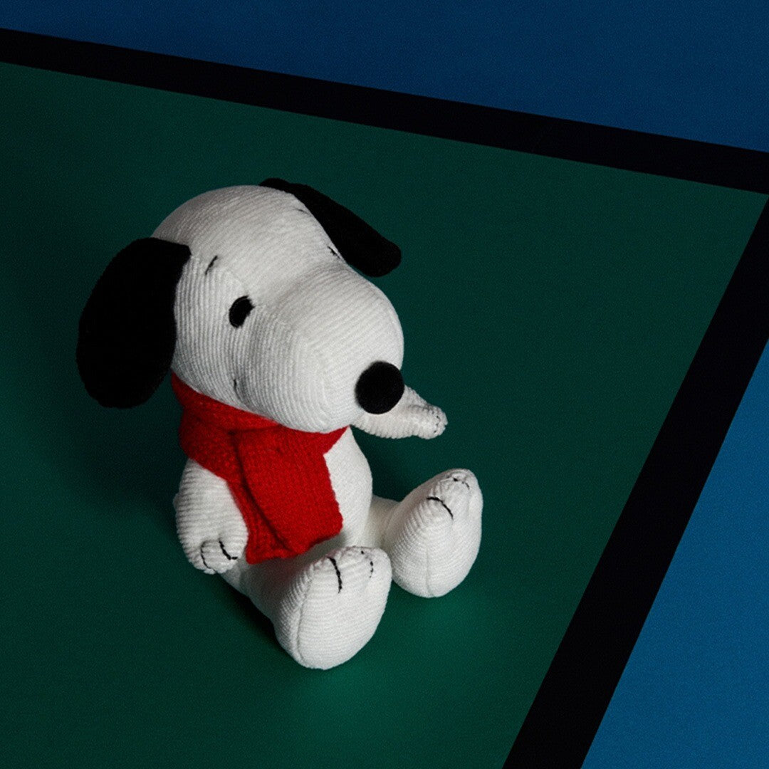 Pluchen knuffelhond Snoopy met rode sjaal zittend op een groene ondergrond.