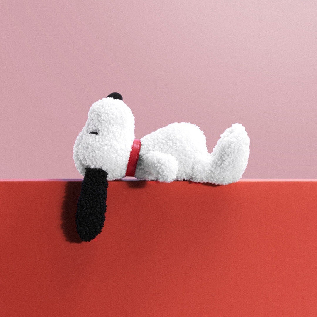 bon ton toys pluchen Snoopy knuffel ligt op een rode rand met een roze achtergrond.