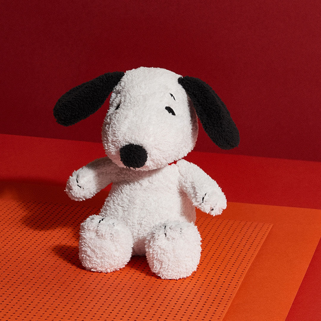 Bon ton toys pluchen knuffelhond Snoopy zittend op een oranje en rode ondergrond.